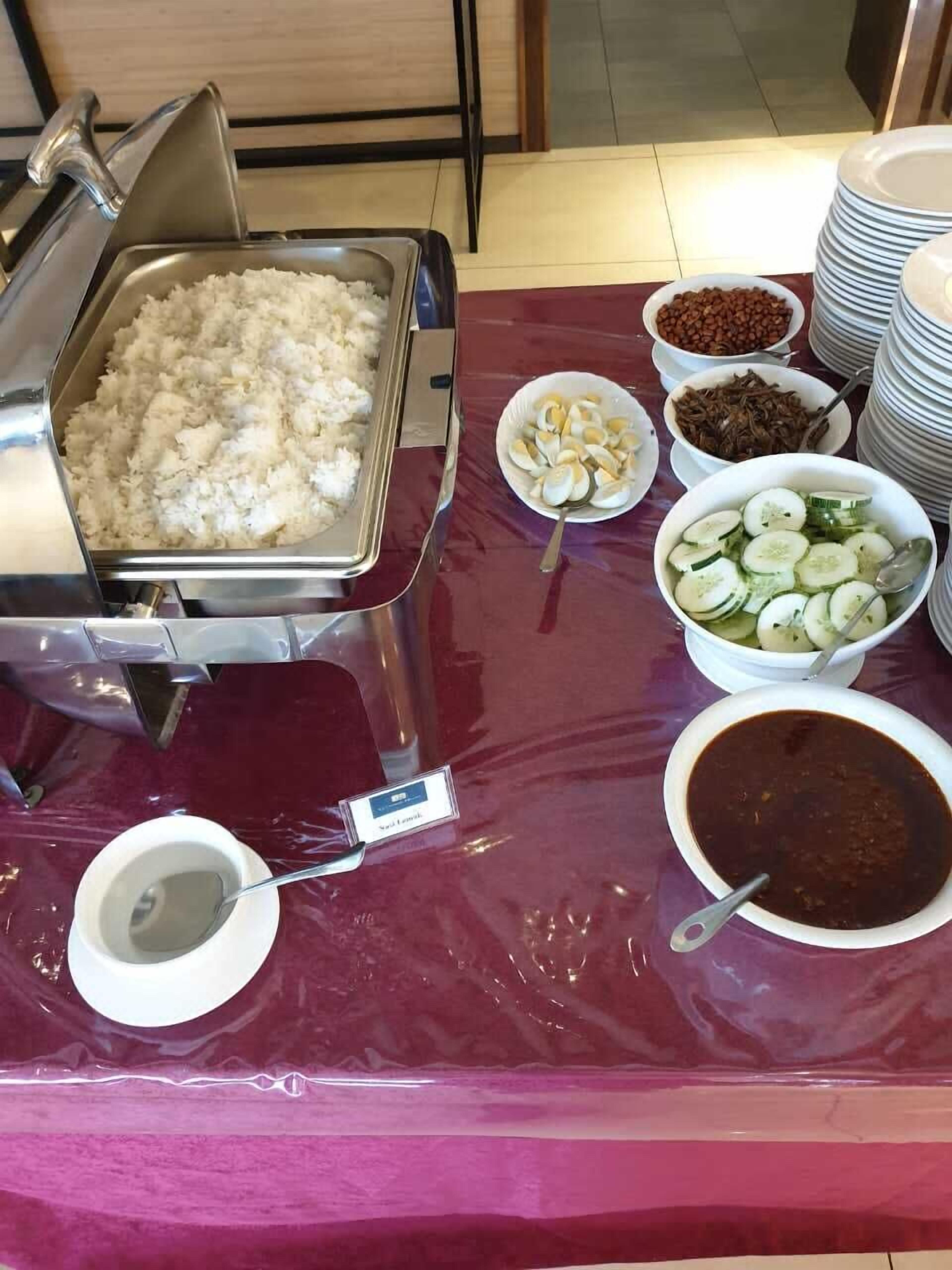 A buffet table with various food items including rice, eggs, cucumbers, and a bowl of sauce.