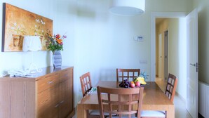 A dining area with a wooden table, four chairs, a vase with flowers, and a telephone on a wooden cabinet.