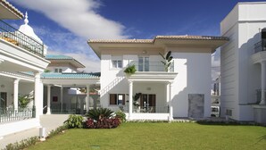 A white building with a covered patio, a small garden, and a clear blue sky.