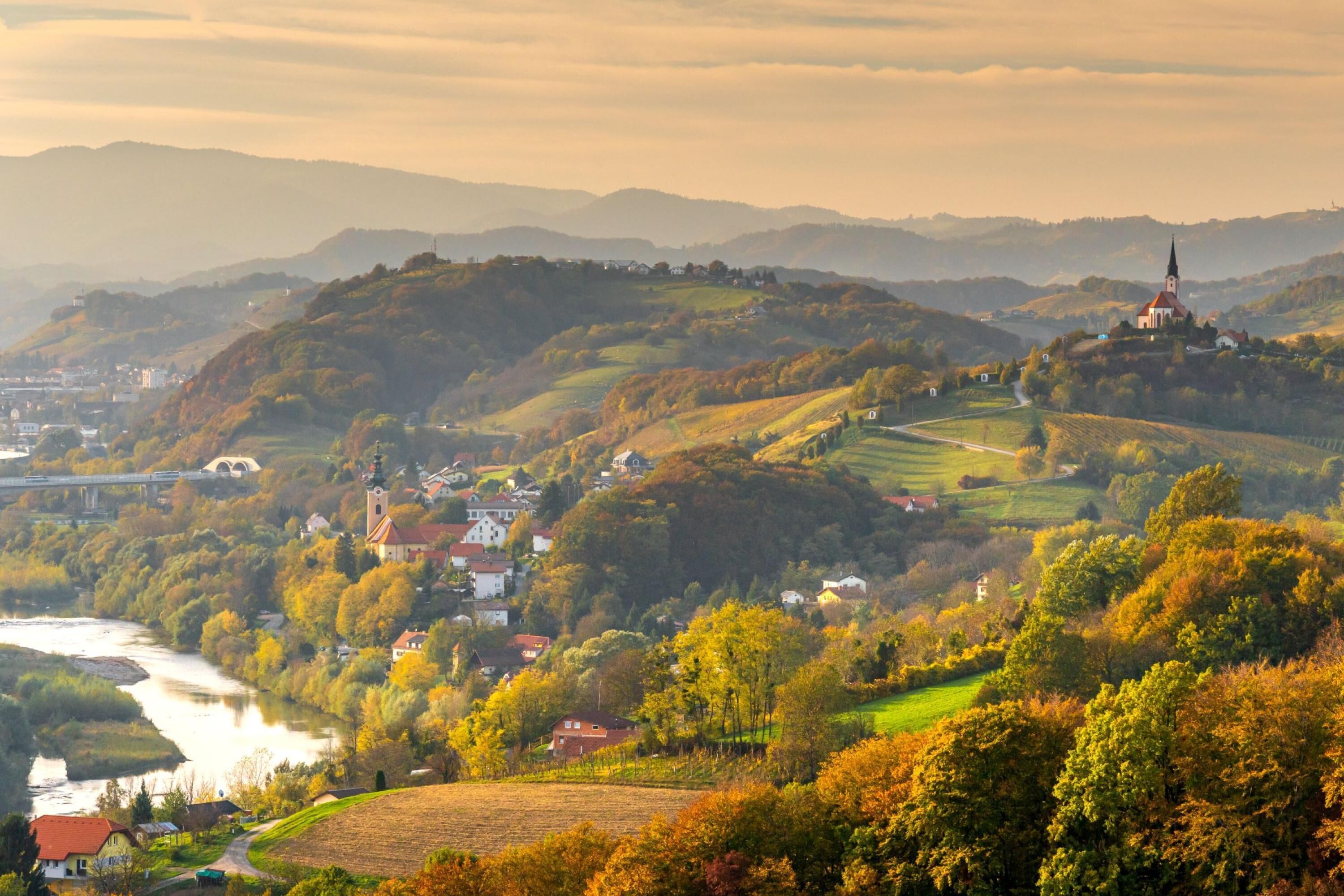 A scenic landscape with rolling hills, a river, and a church.