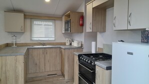Eine kleine Küche mit Holzschränken, einem Gasherd, einer Mikrowelle und einem Kühlschrank.