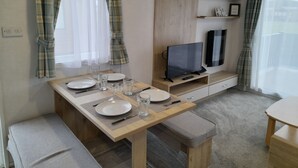 Ein gemütlicher Wohnraum mit Essbereich, einem Fernseher und einem kleinen Regal mit Dekoration.