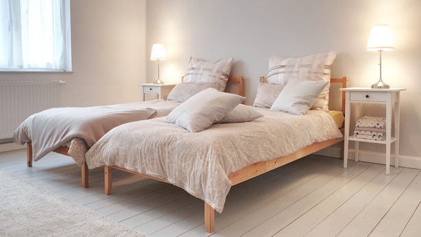 A double bed with a wooden frame, two bedside tables with lamps, a window with sheer curtains, and a radiator. - Chic & bright apartment in Mülheim an der Ruhr (Mülheim an der Ruhr)