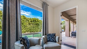 Een kamer met twee fauteuils, uitzicht op een zwembad en een deur naar een buitenruimte met een overdekt terras.