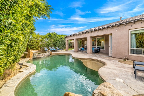 A swimming pool with a stone edge, surrounded by a patio with outdoor furniture.