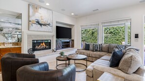 Een moderne woonkamer met een open haard, comfortabele zithoek en een groot raam met uitzicht op groen.