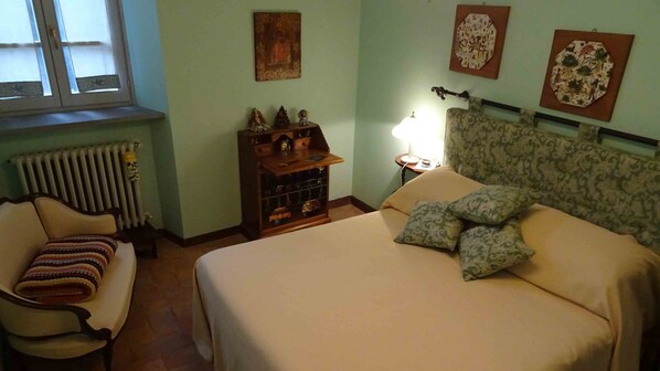 Un dormitorio con cama, una silla, una mesita de noche y un radiador.