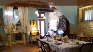 On aperçoit un coin repas avec une table dressée pour quatre personnes, entourée de chaises. Un coin cuisine, avec un four et des placards, est visible sur la gauche.