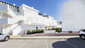 Ein modernes, weißes Gebäude mit Parkplatz, Treppe und einer kleinen Grünfläche.
