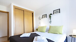 Ein Hotelzimmer mit einem Bett, einem Holzschrank, einem kleinen Tisch und einem an der Wand befestigten Regal mit Pflanze und Bilderrahmen.