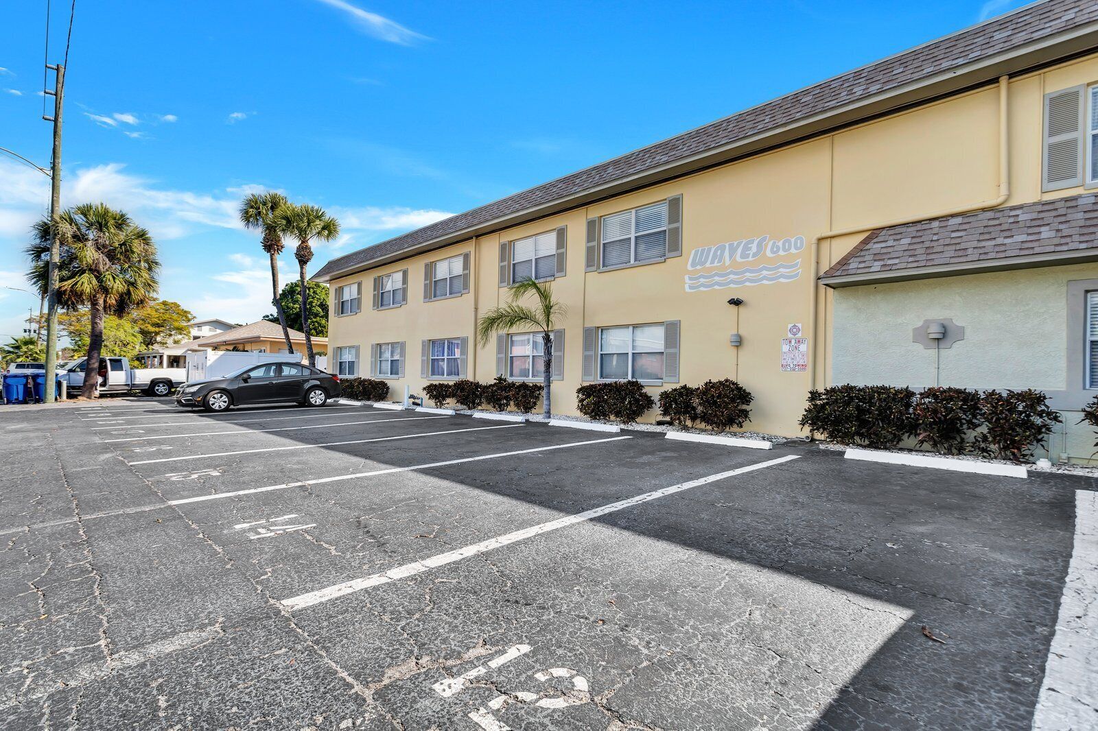 A parking lot with marked spaces, a building with a sign reading "WAVES 600", and a clear blue sky.