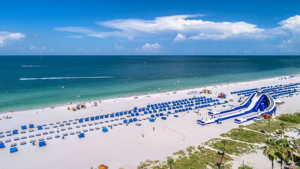A beach with a water slide and numerous blue lounge chairs. - Walk to Beach & Dining | Condo with Pool (St. Pete Beach)