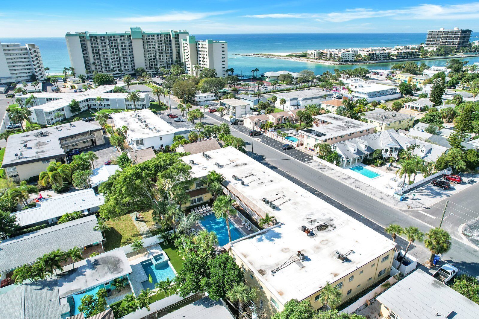 Vista aérea de una zona residencial costera con varios edificios, una piscina y una vista despejada del océano.