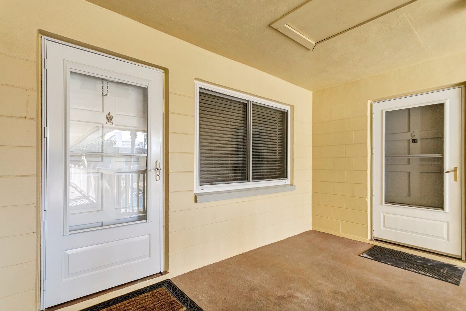 A hallway with a beige wall, a white door with a glass panel, a window with blinds, and a carpeted floor.
