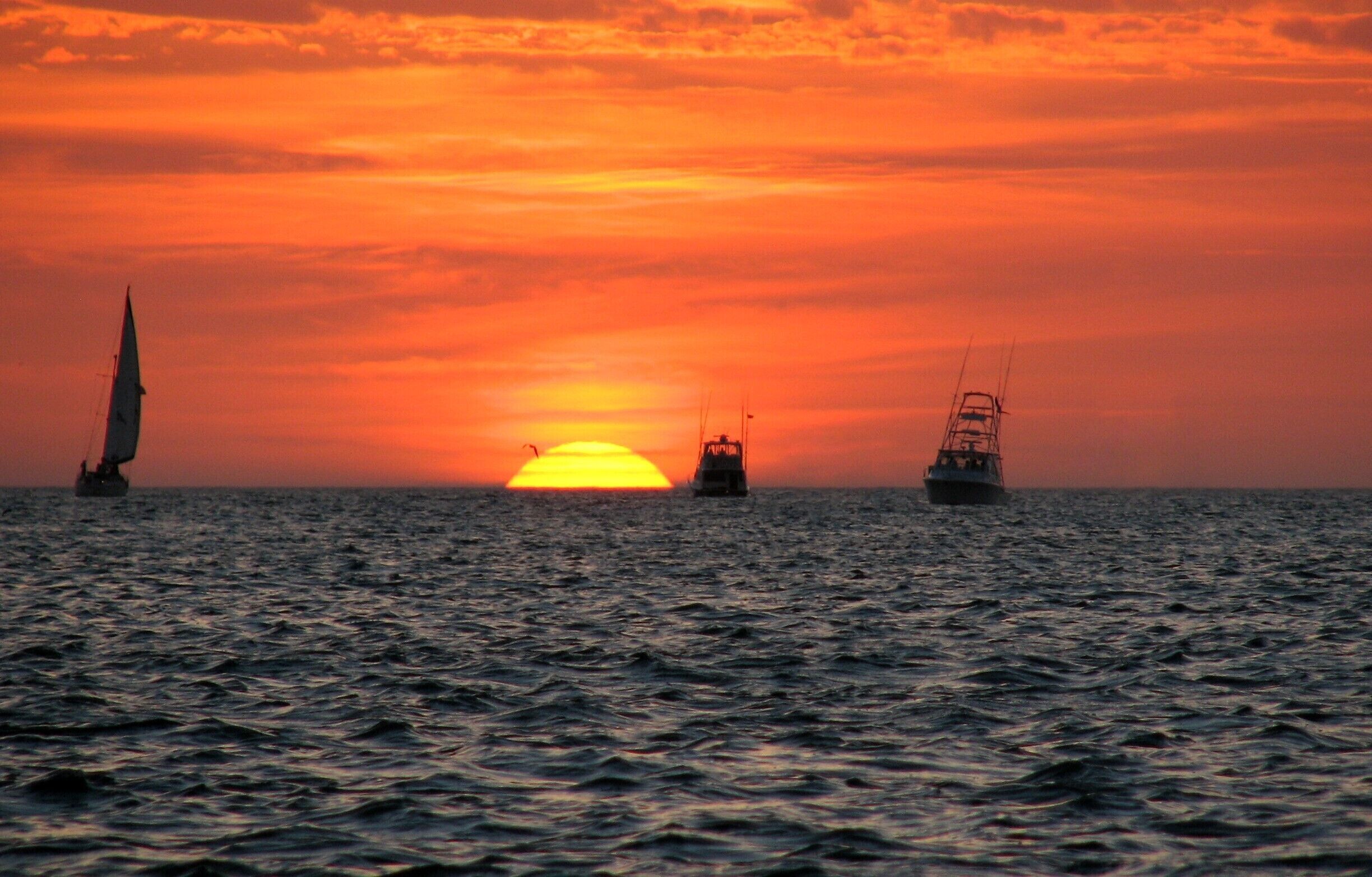 Un atardecer sobre el océano con tres veleros.