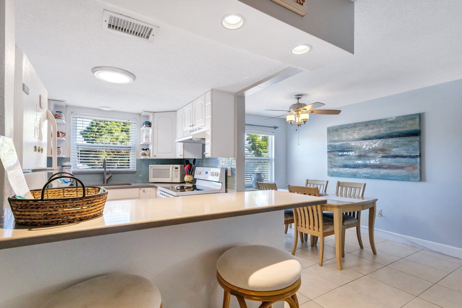 Une cuisine moderne avec des meubles blancs, un îlot central et un coin repas comprenant des chaises et une table en bois.