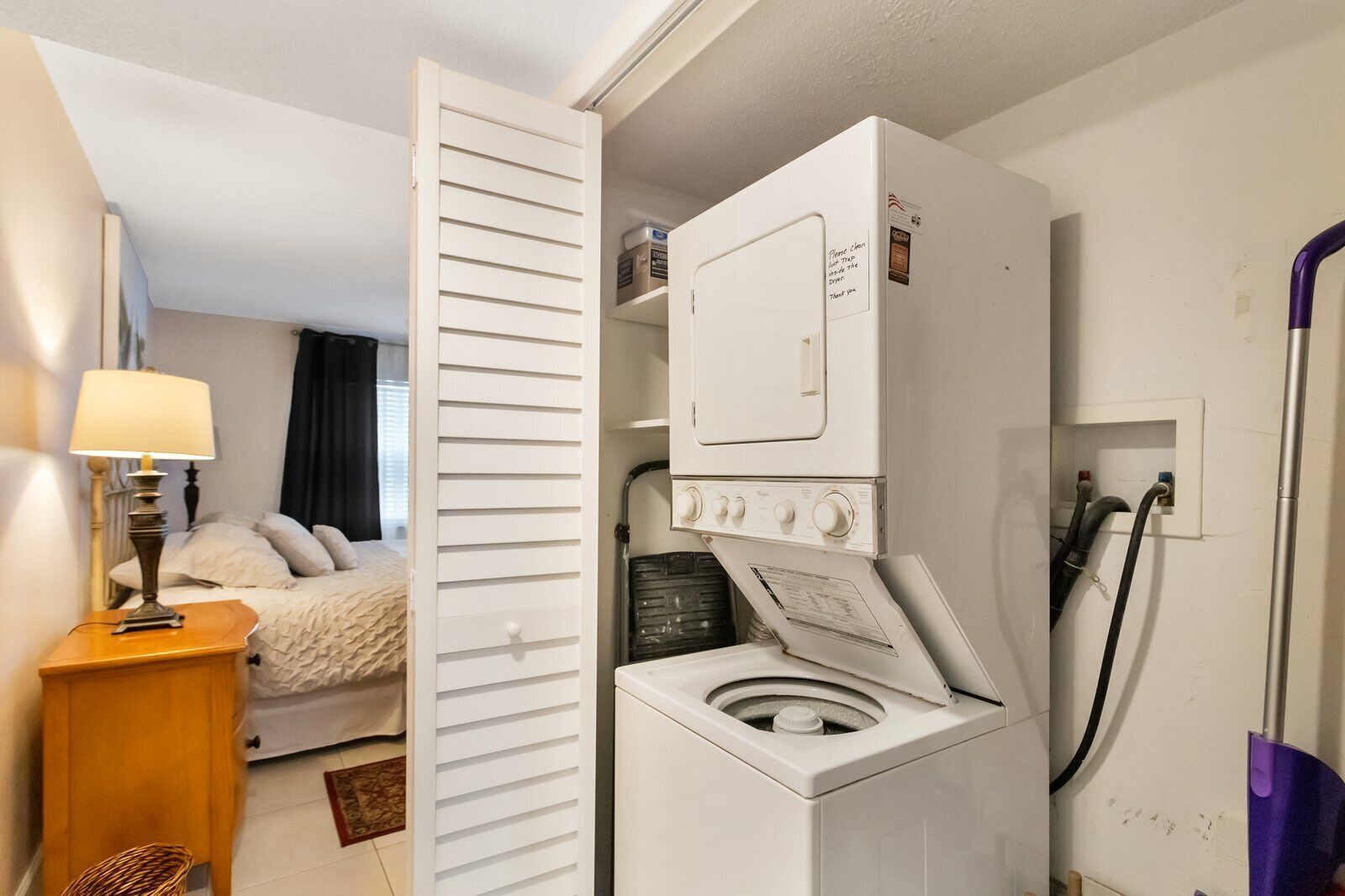 Habitació d'hotel senzilla amb un llit, una taula de nit, una làmpada, una rentadora i un aspirador.