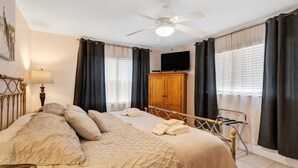 A bedroom with a bed, a ceiling fan, a TV, and a wardrobe. - Walk to Beach & Dining | Condo with Pool (St. Pete Beach)
