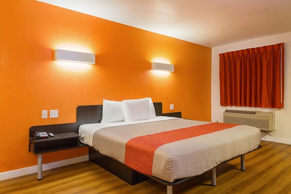 A hotel room with a bed, a nightstand, a phone, and a wall-mounted light fixture. - Motel6 Garland, TX - Northeast Dallas (Garland)