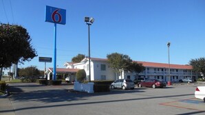 A parking lot with a CarMax sign, a building with a red roof, and several parked cars. - Motel6 Garland, TX - Northeast Dallas (Garland)