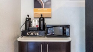 A coffee station with a coffee machine, cups, and a microwave on a counter. - Motel6 Garland, TX - Northeast Dallas (Garland)
