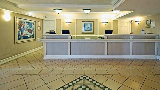 A reception area with a reception desk, two computer stations, a large painting on the wall, and a patterned floor. - Motel6 Garland, TX - Northeast Dallas (Garland)