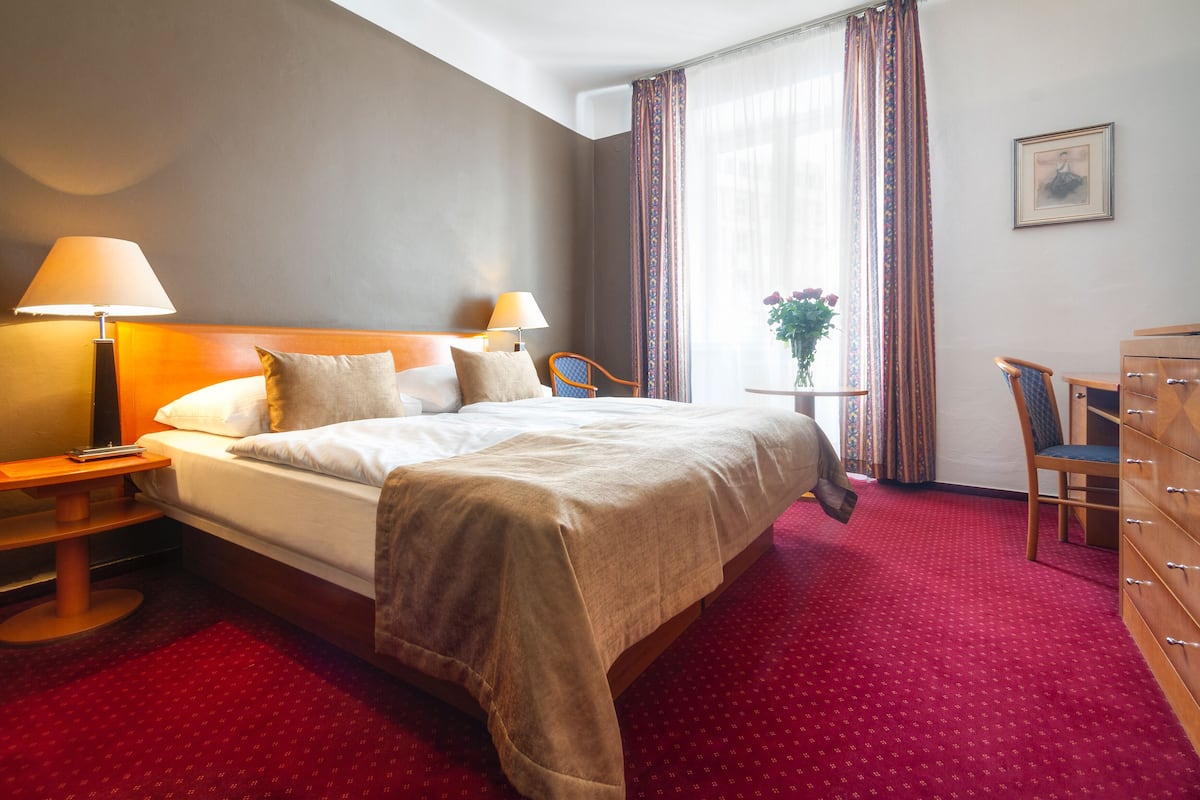 A hotel room with a large bed, two bedside tables with lamps, a dresser, a chair, and a window with curtains.