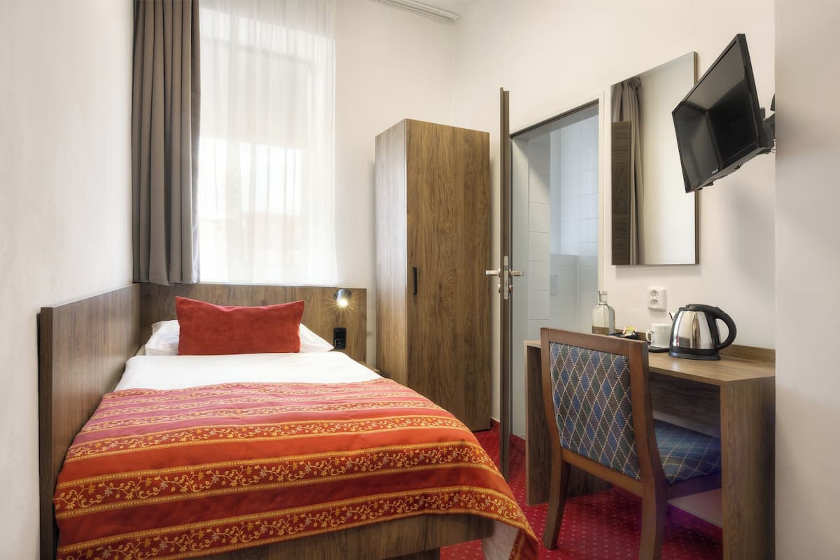 A hotel room with a bed, a desk, a chair, a television, and a wardrobe.