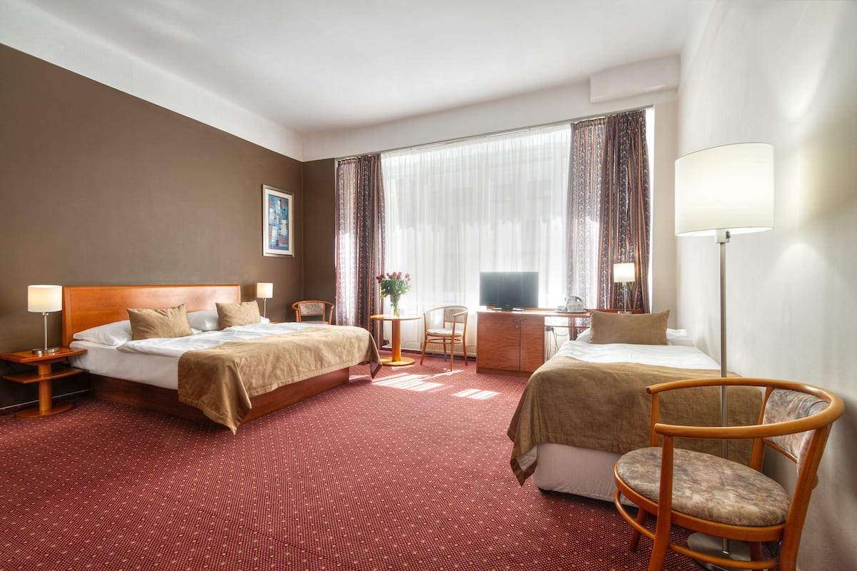 A hotel room with two beds, a desk, a chair, a TV, and a lamp.