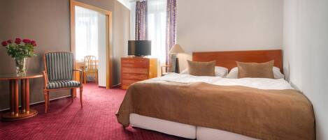 A hotel room with a large bed, a TV, a desk with a chair, and a vase of flowers.