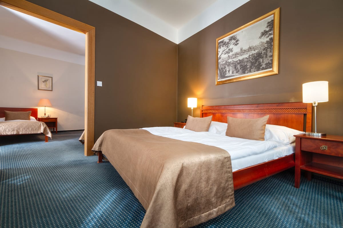 A hotel room with a large bed, two bedside tables, a nightstand, a framed picture on the wall, and a carpeted floor.