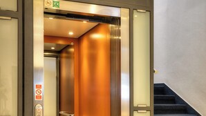An elevator with a digital display, a no-smoking sign, and a door with a 'Harmony' mat. - Hotel Harmony (Prague)