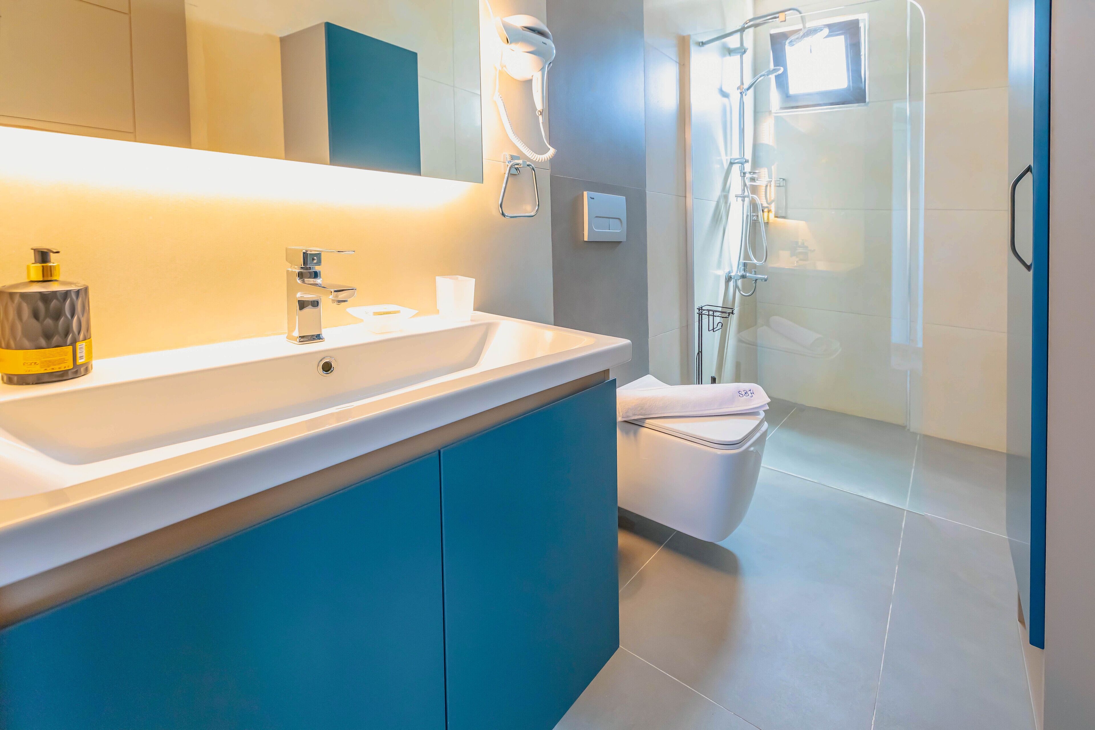 A modern bathroom with a white sink, blue cabinets, a glass shower enclosure, and a toilet.