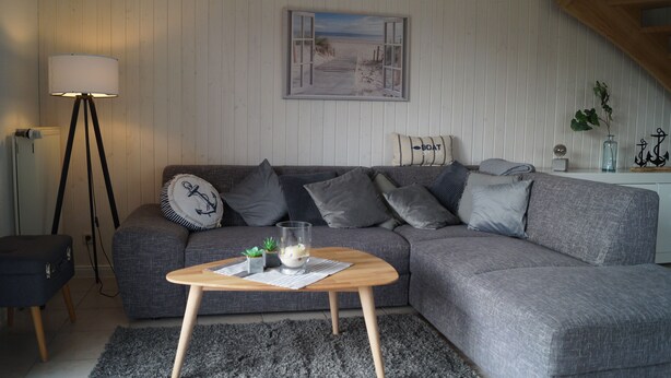 Una sala de estar moderna con un sofá gris, una mesa de centro de madera, una lámpara y un cuadro con una escena de playa.
