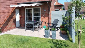 Una casa de ladrillo con techo de tejas rojas, un patio con mesa y sillas, y plantas en macetas.