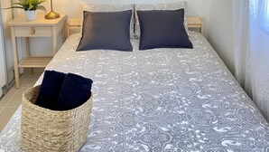 Et soveværelse med en seng, et natbord, en lampe, en plante og et maleri med et strandmotiv på væggen.
