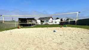 En sandvolleyballbane med net, omgivet af huse og et overdækket siddeområde.