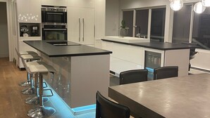 Een moderne keuken met een centraal eiland, barkrukken en een eettafel met stoelen.