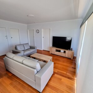 Una sala de estar moderna con un sofá modular, una mesa de centro de madera, un televisor sobre un mueble de madera y piso de madera.