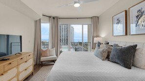 A hotel room with a bed, a TV, a dresser, and a balcony with a view of the city.