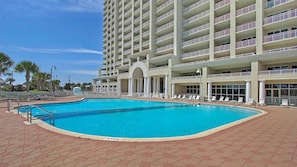 Un hotel con una amplia piscina exterior, varios balcones y un cielo azul despejado.