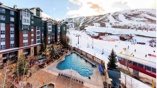 A hotel with a pool, ski slopes, and a mountainous backdrop.