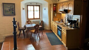 A kitchen with wooden cabinets, a dining table with chairs, a window, and a radiator. - Romantic vacation apartment in a historic castle for 3-4 people (Nürnberg)
