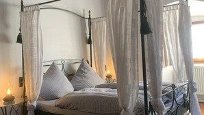 A four-poster canopy bed with a white bedspread and pillows, a bedside table with a lamp, and a patterned rug on the floor. - Romantic vacation apartment in a historic castle for 3-4 people (Nürnberg)