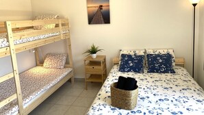 Ein Schlafraum mit Etagenbetten, einem Einzelbett, einem kleinen Tisch mit Pflanze und einem Wandbild.