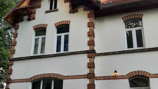 Un edificio a due piani con facciata simmetrica, caratterizzato da un ingresso centrale con porta e gradini, affiancato da finestre con stipiti bianchi e dettagli in mattoni.