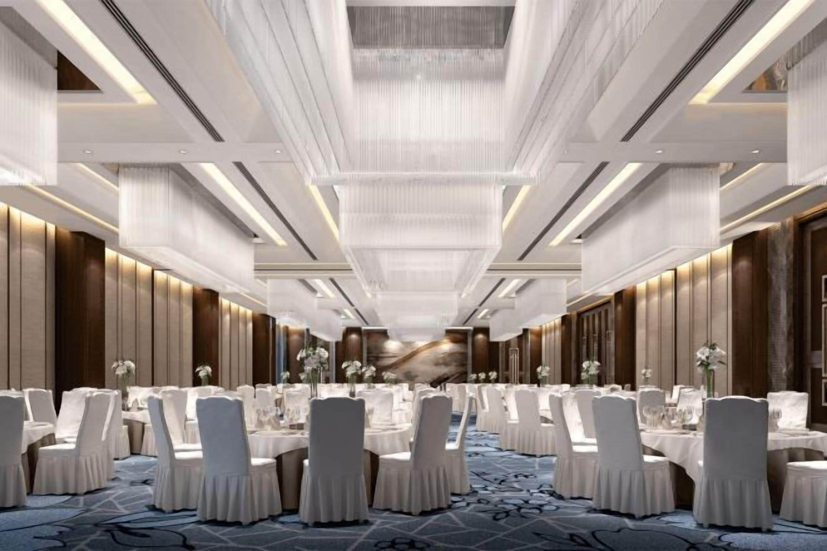 Une salle de banquet spacieuse, dotée de tables et de chaises rondes, d’un plafond haut avec un luminaire central et d’un tapis à motifs.