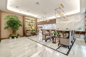 A modern lobby with a large plant, seating area, and a reception desk.