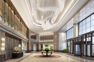 A spacious lobby with a central reception desk, large windows, and a modern chandelier.