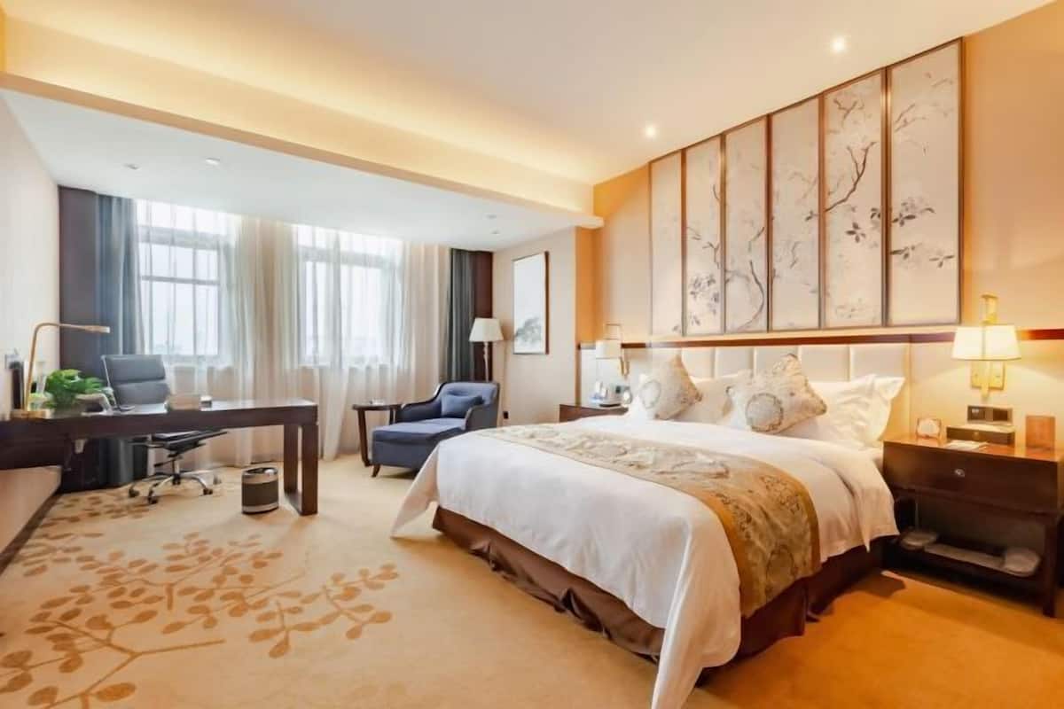 A hotel room with a large bed, a desk with a chair, a small table, and a nightstand.